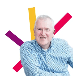 Simon Parsons, wearing a pale blue shirt leaning forward and looking happy. He has a multicoloured spark behind him.